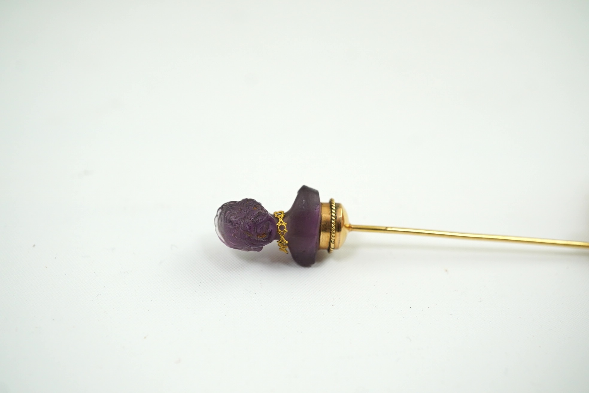 A 19th century French? gold and amethyst set stick pin, the stone carved as the bust of a lady, wearing a necklace